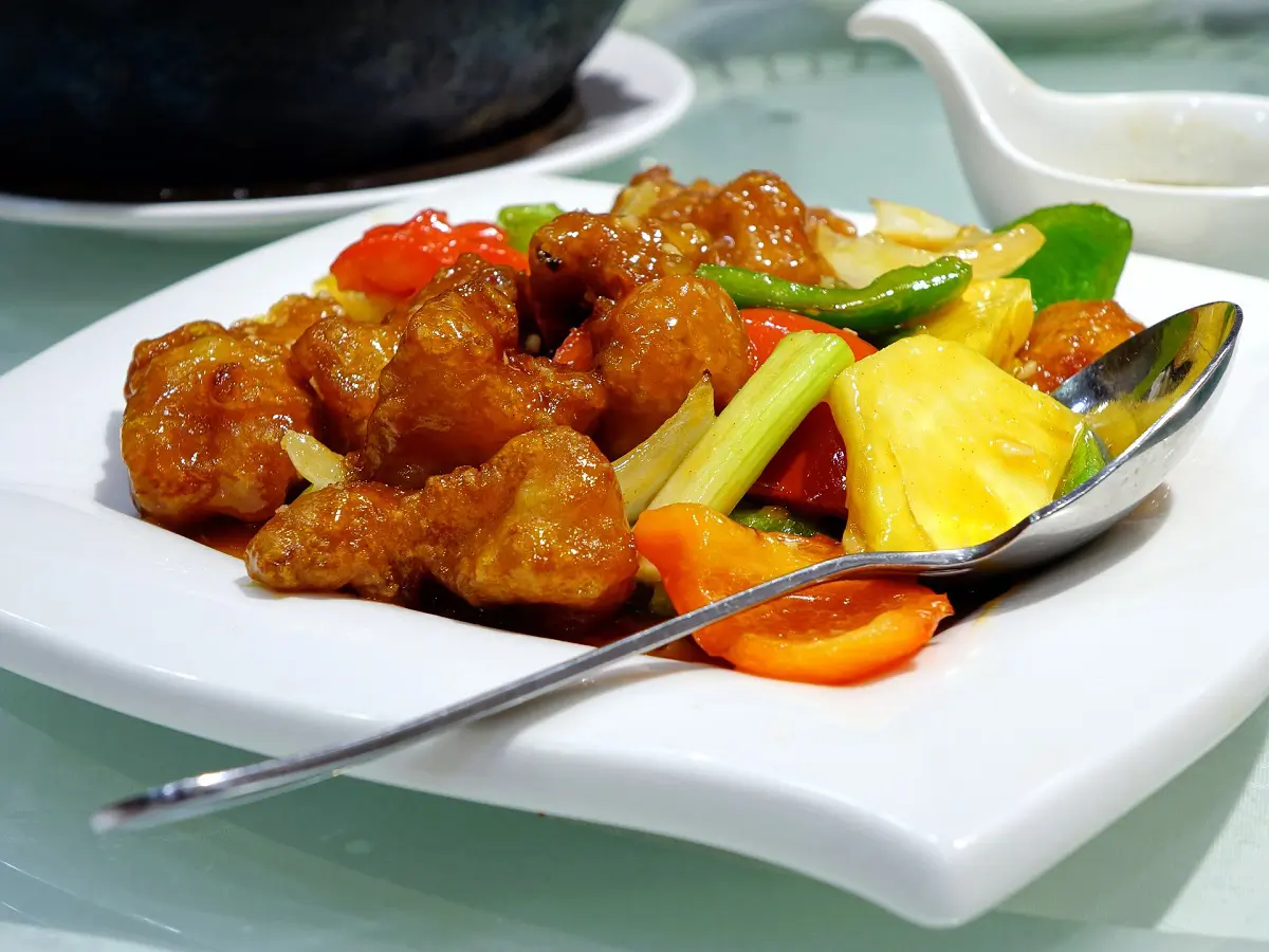 Pineapple sweet and sour pork on a white plate. The meat pieces are coated with glossy sauce, paired with colorful peppers, pineapple at Jade Garden，a Chinese Restaurant in Creston